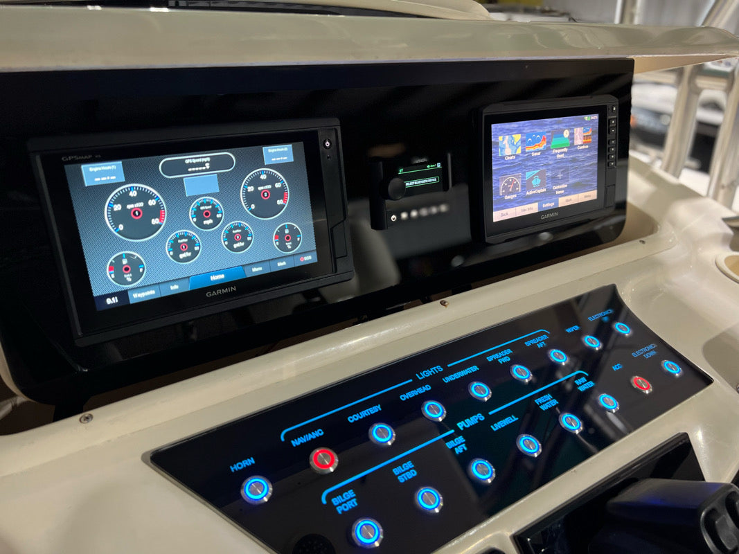 Grady-White Bimini 306 dash panel, angled view of dual Garmin displays and illuminated labeled switch panel
