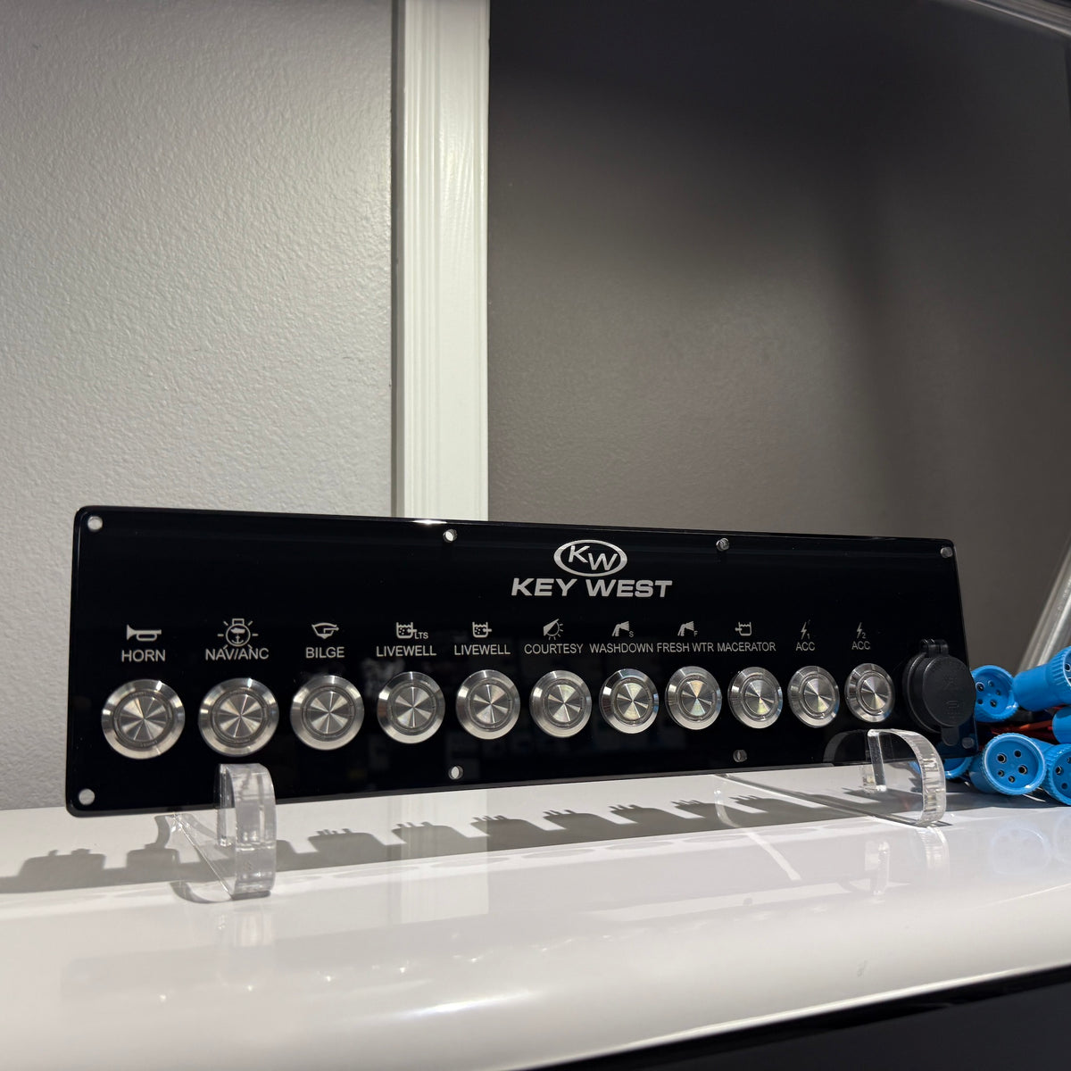 Front view of Key West switch panel on clear stand showing logo, row of metal knobs and labeled controls