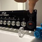 Key West switch panel front angle showing stainless knobs, QC3.0 USB ports, mounting holes and acrylic stand.