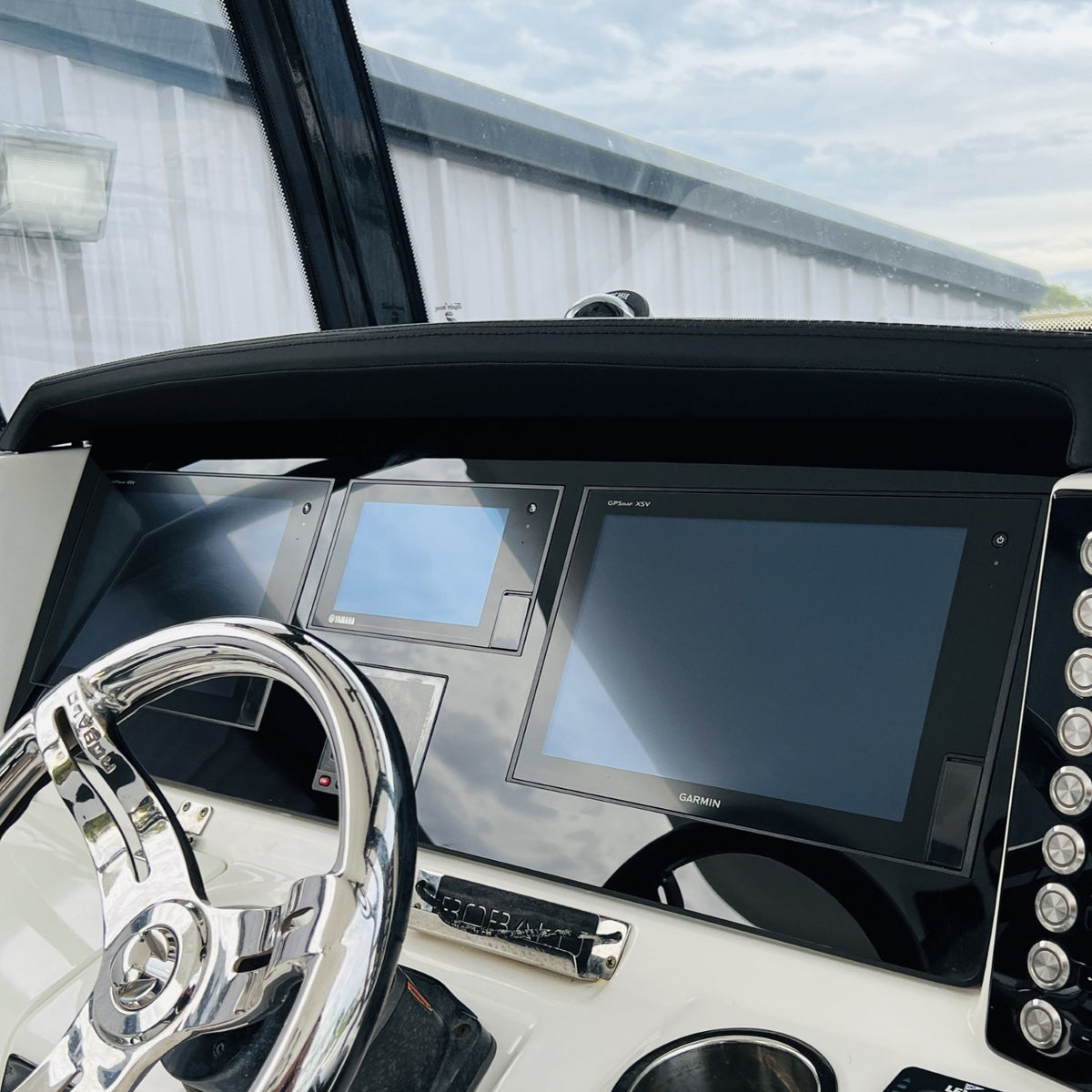 Close-up Robalo helm dash showing Garmin and Yamaha screens, stainless wheel and vertical round switches