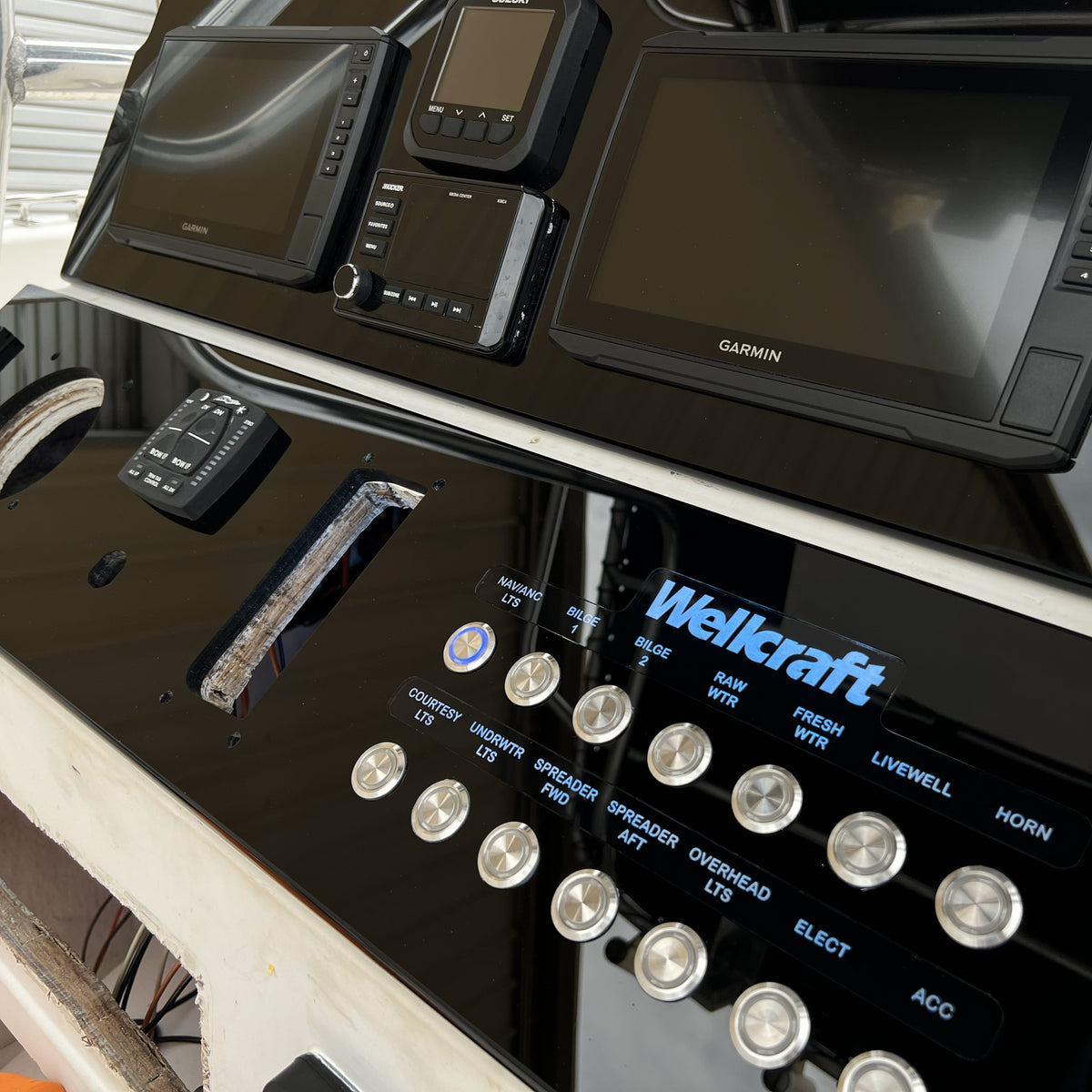 Wellcraft 210 dash panel angled view showing dual Garmin displays, stainless push buttons and cutouts.